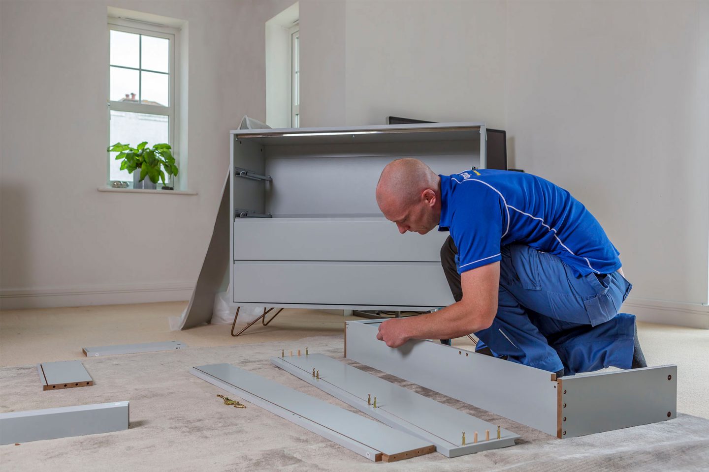 An Aspect handyman assembling a drawer of a flat-pack chest of drawers that has been partially build behind him.