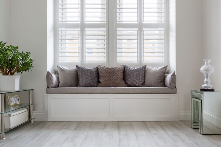 A bespoke-built window seat, covered in cushions, in the bay of a lounge window.