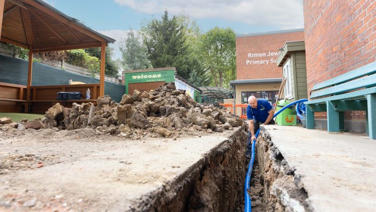 An Aspect tradesperson laying new water supply pipes in a trench dug in a school playground.