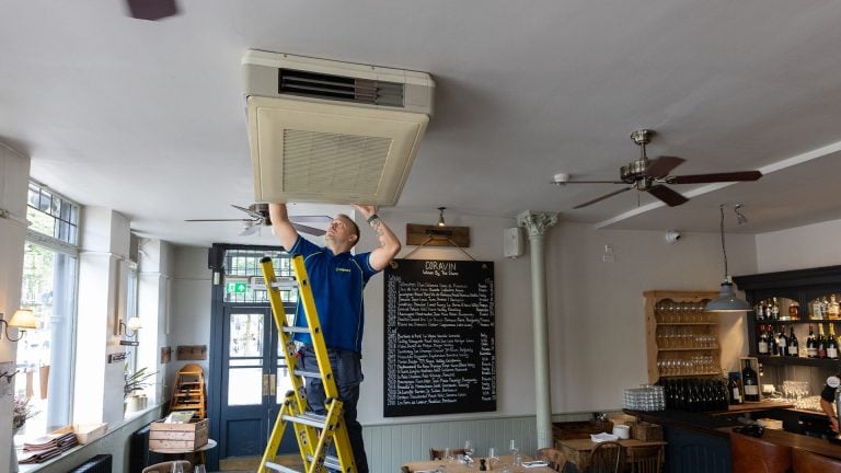 An Aspect air con engineer services a ceiling air conditioning unit in a restaurant.