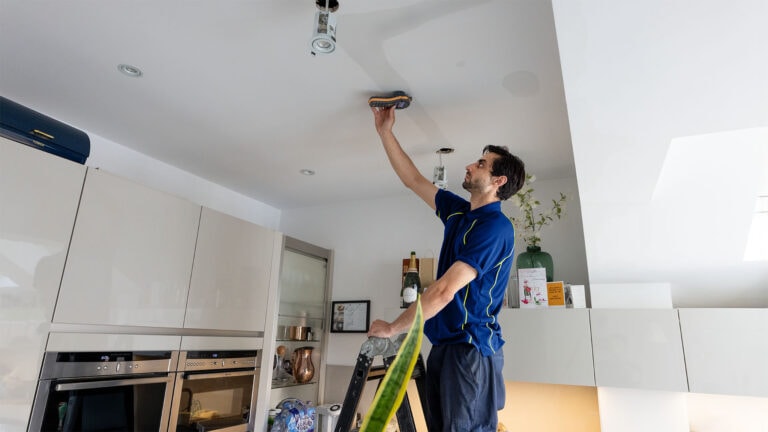 An Aspect tradesperson using a moisture meter on a section of kitchen ceiling that appears to be water damaged