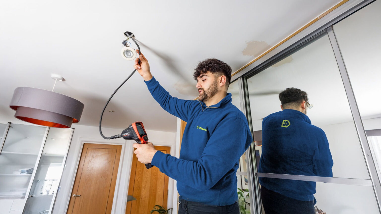 An Aspect tradesperson investigating the cause of damp patches on a ceiling by using a borescope inserted into a light fixing