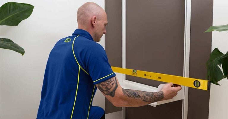 An Aspect handyman using a spirit level to check a shelf being fitted to a wall.