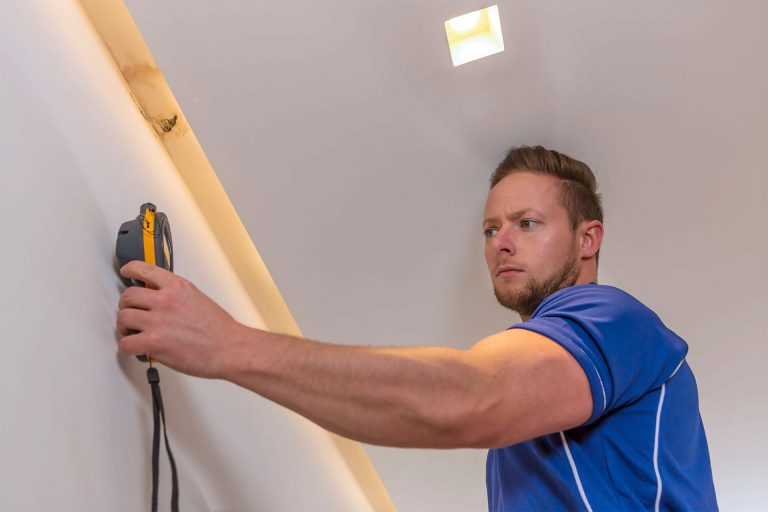 An Aspect tradesperson using a moisture meter on a patch of mould on a wall as part of a water leak detection process