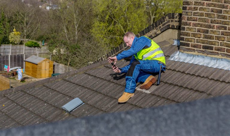 An Aspect roofer performing a roof survey, taking photos on a pitched section of roof.