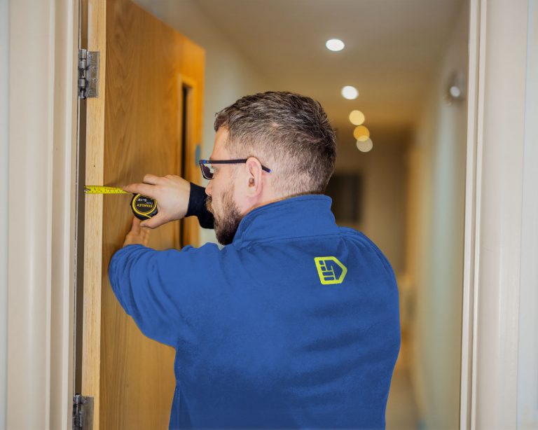 An Aspect fire door technician measures a fire door in a block of flat to check it's compliant with regulations.