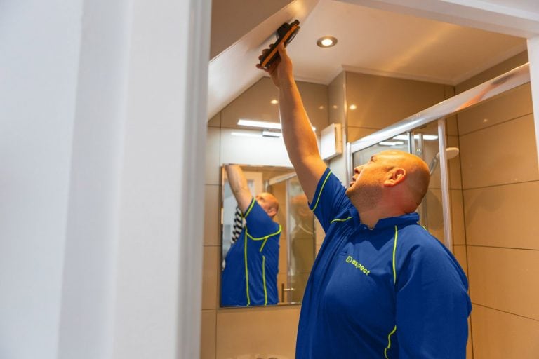 An Aspect damp specialist using a meter to record moisture content levels on a ceiling while carrying out a damp survey in a bathroom without a window.