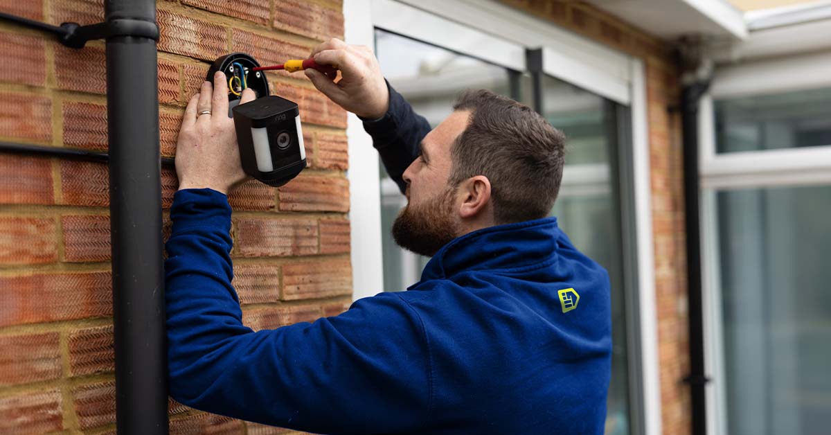 An Aspect electrician fixing a lighting motion sensor to the outdoor wall of a house.