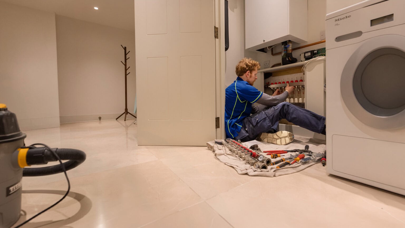 An Aspect heating engineer adjusts an underfloor heating manifold positioned beneath a gas boiler in a domestic property.