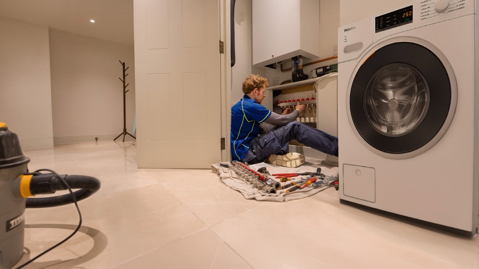 An Aspect heating engineer adjusts an underfloor heating manifold positioned beneath a gas boiler in a domestic property.
