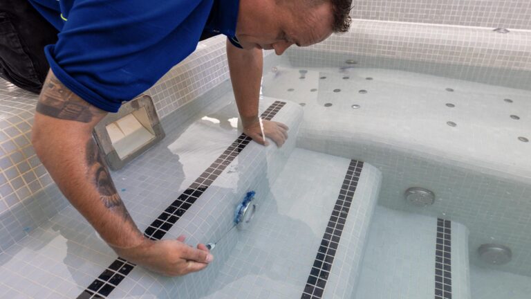 A leak detection specialist uses a syringe to add dye close to a return jet in a swimming pool to test for a leak.